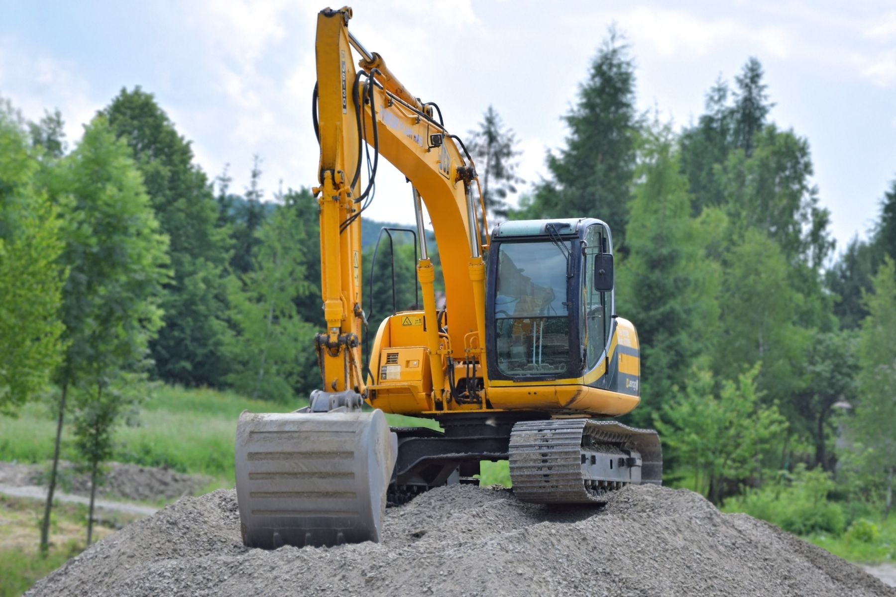 Excavator on gravel with evergreen trees in the background